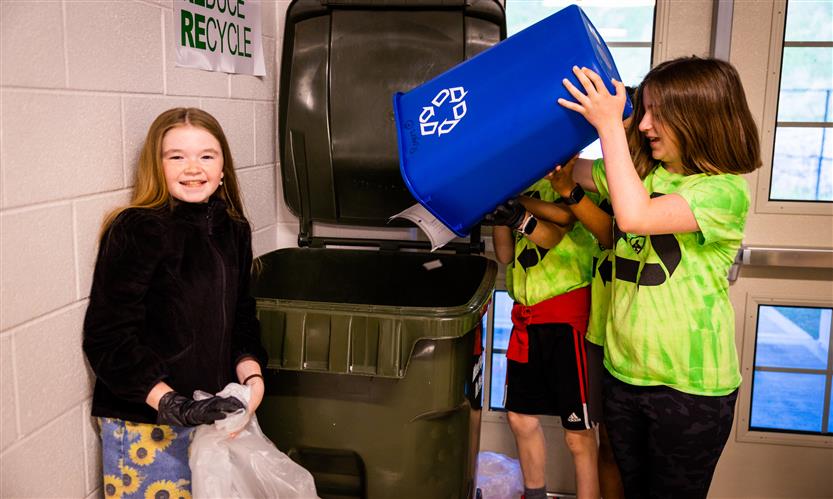 Students help dump a recycling bin into a larger can